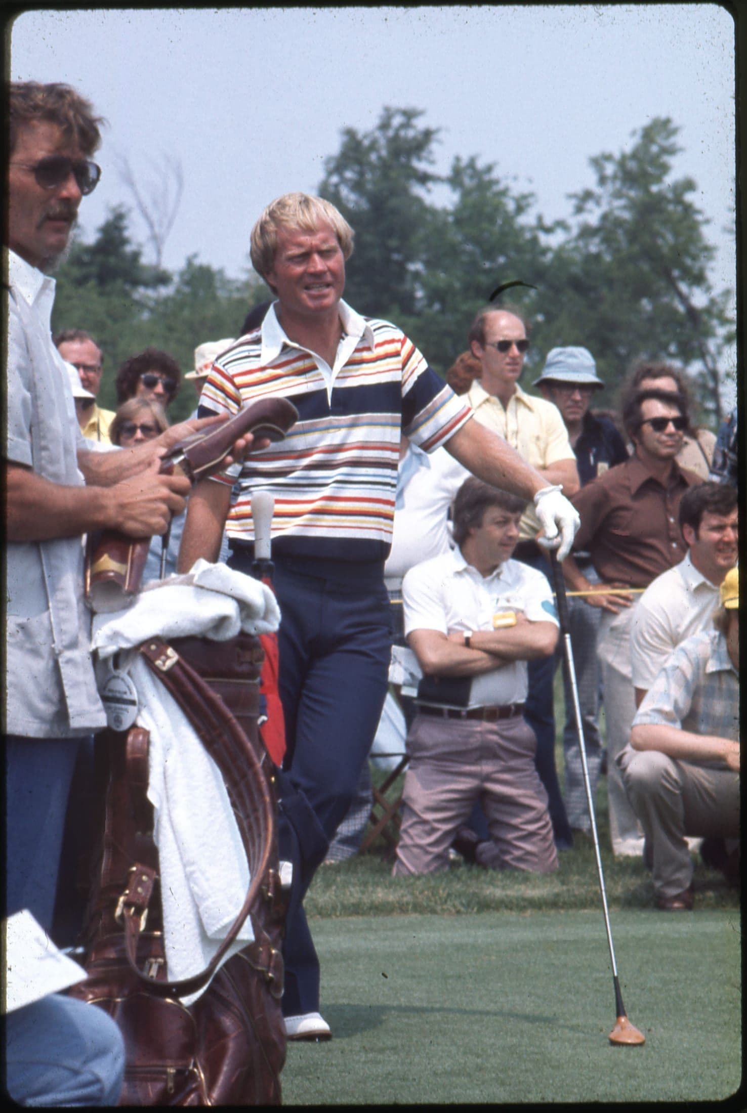 A golfer in a striped shirt walking off the green at a 1970s tournament